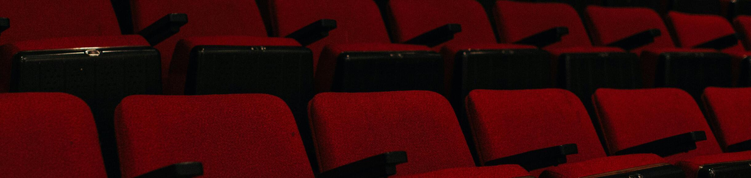 Darkened image of empty red movie theater seats.